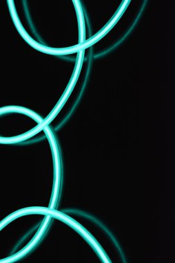 Parlak parlak elektroaydınlatma kabloları, açık yeşil, yeşil, mavi, gök mavisi, turkuaz kalın ışık çizgileri. Neon kaotik çizgiler spiraller, daireler ve kıvrımlar halinde siyah bir arkaplanda dizilir..