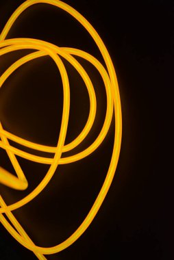 Parlak parlak elektroaydınlatma kabloları, sarı, turuncu, kalın ışık çizgileri. Neon kaotik çizgiler spiraller, daireler ve kıvrımlar halinde siyah bir arkaplanda dizilir..