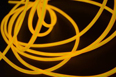 Parlak parlak elektroaydınlatma kabloları, sarı, turuncu, kalın ışık çizgileri. Neon kaotik çizgiler spiraller, daireler ve kıvrımlar halinde siyah bir arkaplanda dizilir..