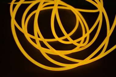 Parlak parlak elektroaydınlatma kabloları, sarı, turuncu, kalın ışık çizgileri. Neon kaotik çizgiler spiraller, daireler ve kıvrımlar halinde siyah bir arkaplanda dizilir..