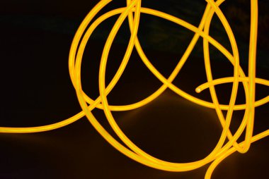 Parlak parlak elektroaydınlatma kabloları, sarı, turuncu, kalın ışık çizgileri. Neon kaotik çizgiler spiraller, daireler ve kıvrımlar halinde siyah bir arkaplanda dizilir..