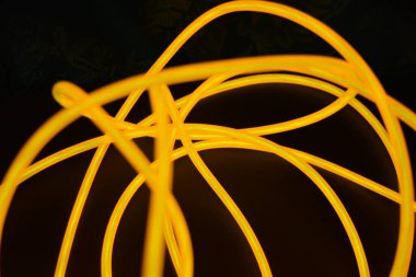 Parlak parlak elektroaydınlatma kabloları, sarı, turuncu, kalın ışık çizgileri. Neon kaotik çizgiler spiraller, daireler ve kıvrımlar halinde siyah bir arkaplanda dizilir..