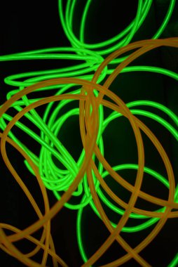 Parlak parlak kablolar, yeşil, limon, kireç, turuncu, turuncu ışık çizgileri. Neon kaotik çizgiler spiraller, daireler ve kıvrımlar halinde siyah bir arkaplanda dizilir..