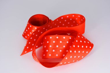 Eşyalar, nesneler, malzemeler ilginç bir şekilde beyaz bir yüzeye serilmiş ve bükülmüştür. Beyaz benekli parlak kırmızı saten kurdeleler beyaz plastik arka planda yer almaktadır..