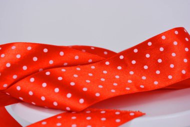 Eşyalar, nesneler, malzemeler ilginç bir şekilde beyaz bir yüzeye serilmiş ve bükülmüştür. Beyaz benekli parlak kırmızı saten kurdeleler beyaz plastik arka planda yer almaktadır..