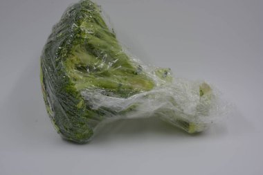 Health, healthy foods, vegetables, healthy eating. Cabbage, green healthy broccoli wrapped in cling film and placed on a white matte background. clipart