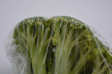 Health, healthy foods, vegetables, healthy eating. Cabbage, green healthy broccoli wrapped in cling film and placed on a white matte background. clipart