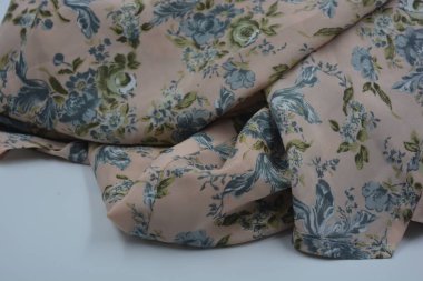 Alışılmadık, parlak yaz kumaşı. Beyaz, ince sentetik, mavi çiçekli ipek kumaş, yeşil yapraklar beyaz plastik arka planda yer almaktadır..