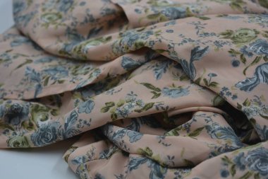 Alışılmadık, parlak yaz kumaşı. Beyaz, ince sentetik, mavi çiçekli ipek kumaş, yeşil yapraklar beyaz plastik arka planda yer almaktadır..