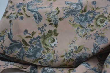 Alışılmadık, parlak yaz kumaşı. Beyaz, ince sentetik, mavi çiçekli ipek kumaş, yeşil yapraklar beyaz plastik arka planda yer almaktadır..