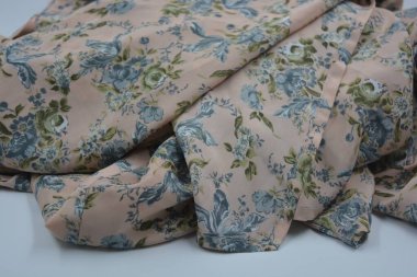 Alışılmadık, parlak yaz kumaşı. Beyaz, ince sentetik, mavi çiçekli ipek kumaş, yeşil yapraklar beyaz plastik arka planda yer almaktadır..