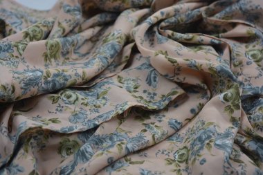 Alışılmadık, parlak yaz kumaşı. Beyaz, ince sentetik, mavi çiçekli ipek kumaş, yeşil yapraklar beyaz plastik arka planda yer almaktadır..