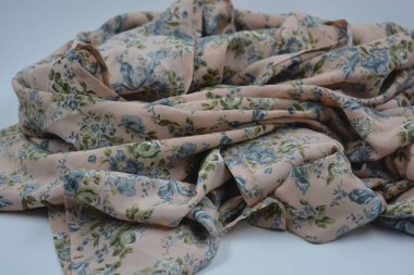 Alışılmadık, parlak yaz kumaşı. Beyaz, ince sentetik, mavi çiçekli ipek kumaş, yeşil yapraklar beyaz plastik arka planda yer almaktadır..