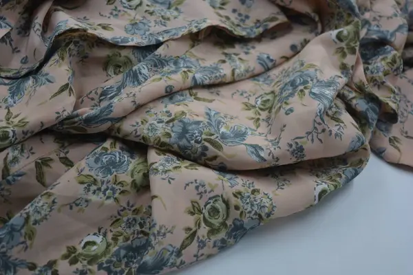 Alışılmadık, parlak yaz kumaşı. Beyaz, ince sentetik, mavi çiçekli ipek kumaş, yeşil yapraklar beyaz plastik arka planda yer almaktadır..