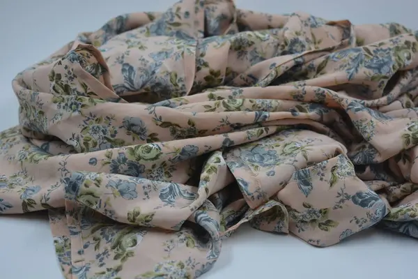 Alışılmadık, parlak yaz kumaşı. Beyaz, ince sentetik, mavi çiçekli ipek kumaş, yeşil yapraklar beyaz plastik arka planda yer almaktadır..