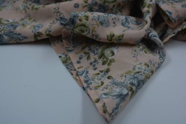 Alışılmadık, parlak yaz kumaşı. Beyaz, ince sentetik, mavi çiçekli ipek kumaş, yeşil yapraklar beyaz plastik arka planda yer almaktadır..