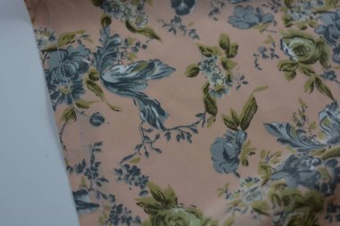 Alışılmadık, parlak yaz kumaşı. Beyaz, ince sentetik, mavi çiçekli ipek kumaş, yeşil yapraklar beyaz plastik arka planda yer almaktadır..