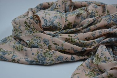 Alışılmadık, parlak yaz kumaşı. Beyaz, ince sentetik, mavi çiçekli ipek kumaş, yeşil yapraklar beyaz plastik arka planda yer almaktadır..