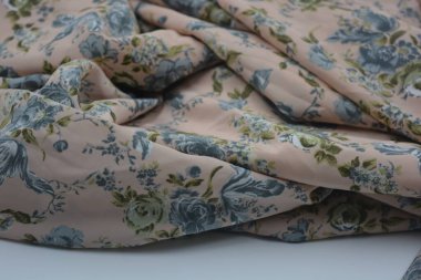 Alışılmadık, parlak yaz kumaşı. Beyaz, ince sentetik, mavi çiçekli ipek kumaş, yeşil yapraklar beyaz plastik arka planda yer almaktadır..