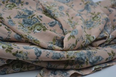 Alışılmadık, parlak yaz kumaşı. Beyaz, ince sentetik, mavi çiçekli ipek kumaş, yeşil yapraklar beyaz plastik arka planda yer almaktadır..