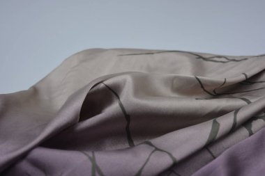 Alışılmadık, parlak ve parıltılı yaz kumaşı. Bej, kum, narin mor, ince sentetik, koyu renk göz kapakları olan ipek kumaş, beyaz plastik arka planda çizgiler var..