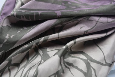 Alışılmadık, parlak ve parıltılı yaz kumaşı. Bej, kum, narin mor, ince sentetik, koyu renk göz kapakları olan ipek kumaş, beyaz plastik arka planda çizgiler var..