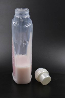 Siyah plastik zemin üzerinde, büyük, şeffaf, pembe bir sıvı ve altın sarısı yuvarlak bir şapka bulunan plastik bir şişe bulunur. Temizlik için sıvı, banyoda yıkanma, çamaşır odası..