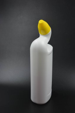Siyah plastik zemin üzerine kıvrımlı boyunlu ve sarı kapaklı beyaz plastik bir şişe yerleştirilir. Plastik şişe banyoyu temizlemek için kullanılır..