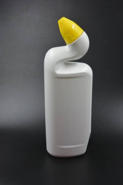 Siyah plastik zemin üzerine kıvrımlı boyunlu ve sarı kapaklı beyaz plastik bir şişe yerleştirilir. Plastik şişe banyoyu temizlemek için kullanılır..