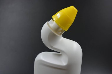 Siyah plastik zemin üzerine kıvrımlı boyunlu ve sarı kapaklı beyaz plastik bir şişe yerleştirilir. Plastik şişe banyoyu temizlemek için kullanılır..