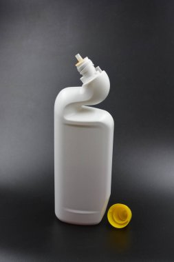 A white plastic bottle with a curved neck and a yellow cap is placed on a black plastic background. A plastic bottle is used for cleaning in the bathroom. clipart