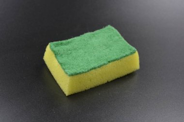 Yeşil kaba bulaşık yüzeyi olan küçük sarı bir sünger siyah, mat plastik bir arka plana yerleştirilir..