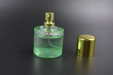 Kadın kıyafetleri, parfümler, parfümler, hoş kokular. Yeşil sıvı parfümlü cam şişe, siyah plastik zemin üzerine yerleştirilmiş altın kaplama ve altın sprey..