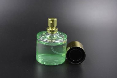Kadın kıyafetleri, parfümler, parfümler, hoş kokular. Yeşil sıvı parfümlü cam şişe, siyah plastik zemin üzerine yerleştirilmiş altın kaplama ve altın sprey..