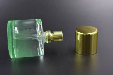 Kadın kıyafetleri, parfümler, parfümler, hoş kokular. Yeşil sıvı parfümlü cam şişe, siyah plastik zemin üzerine yerleştirilmiş altın kaplama ve altın sprey..