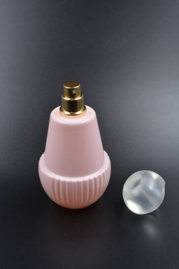 Kadın eşyaları, parfümler, hoş kokular. Hoş bir çilek parfümlü zarif bir pembe şişe, bir mat beyaz plastik şapka ve bir altın püskürtücü siyah plastik arka planda düzenlenir..