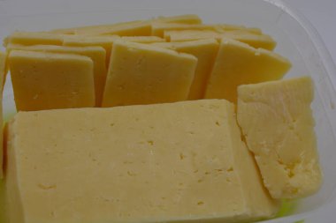 Dilimlenmiş lezzetli peynir dilimli, yemek kalitesinde plastik bir kap beyaz bir mat arka planına yerleştirilir..