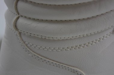 Kumaş arka plan, beyaz deri kumaştan malzemeler, plastik, kauçuk. Beyaz yüzey beyaz ipliklerle dikilmiş, malzeme yıpranmış..