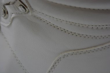 Kumaş arka plan, beyaz deri kumaştan malzemeler, plastik, kauçuk. Beyaz yüzey beyaz ipliklerle dikilmiş, malzeme yıpranmış..