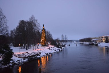 Güzel manzara, yeni yıl için süslenmiş göl kıyısı, Finlandiya 'nın Varkaus şehrinde Noel. Büyük yeşil bir Noel ağacı parlayan ampullerde, Yeni Yıl çelenklerinde, alışılmadık ağaçlarda, binalarda ve sahildeki yapılarda duruyor..