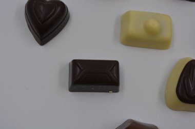 Güzel, alışılmadık ve lezzetli tatlılar, çikolatalar. Beyaz plastik arka planda siyah, süt ve beyaz çikolatadan yapılmış Belçika tatlısı bulunur..
