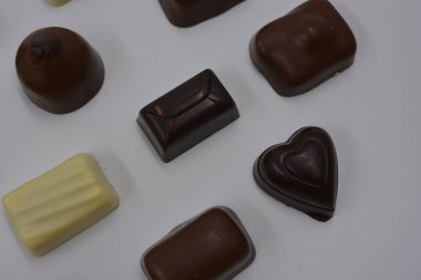 Güzel, alışılmadık ve lezzetli tatlılar, çikolatalar. Beyaz plastik arka planda siyah, süt ve beyaz çikolatadan yapılmış Belçika tatlısı bulunur..