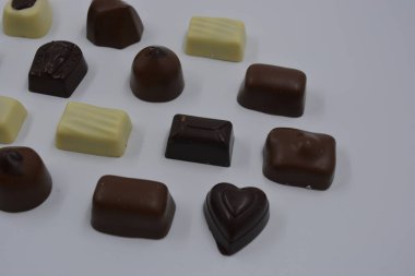 Güzel, alışılmadık ve lezzetli tatlılar, çikolatalar. Beyaz plastik arka planda siyah, süt ve beyaz çikolatadan yapılmış Belçika tatlısı bulunur..