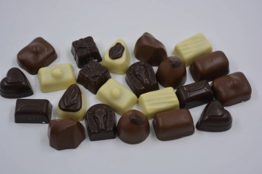 Güzel, alışılmadık ve lezzetli tatlılar, çikolatalar. Beyaz plastik arka planda siyah, süt ve beyaz çikolatadan yapılmış Belçika tatlısı bulunur..