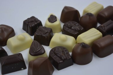 Güzel, alışılmadık ve lezzetli tatlılar, çikolatalar. Beyaz plastik arka planda siyah, süt ve beyaz çikolatadan yapılmış Belçika tatlısı bulunur..