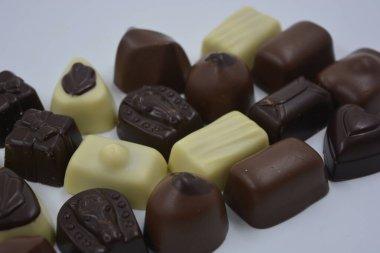 Güzel, alışılmadık ve lezzetli tatlılar, çikolatalar. Beyaz plastik arka planda siyah, süt ve beyaz çikolatadan yapılmış Belçika tatlısı bulunur..