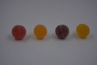 Beyaz şekerle kaplı yuvarlak toplar şeklinde orijinal Finlandiya şekerleri. Sarı, turuncu, kiraz, kırmızı jelibon şekerleri beyaz plastik arka planda bulunur..