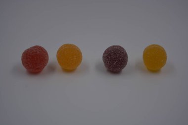 Beyaz şekerle kaplı yuvarlak toplar şeklinde orijinal Finlandiya şekerleri. Sarı, turuncu, kiraz, kırmızı jelibon şekerleri beyaz plastik arka planda bulunur..