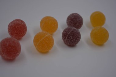 Beyaz şekerle kaplı yuvarlak toplar şeklinde orijinal Finlandiya şekerleri. Sarı, turuncu, kiraz, kırmızı jelibon şekerleri beyaz plastik arka planda bulunur..