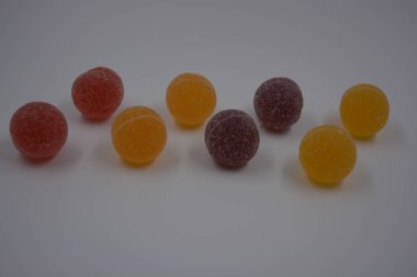 Beyaz şekerle kaplı yuvarlak toplar şeklinde orijinal Finlandiya şekerleri. Sarı, turuncu, kiraz, kırmızı jelibon şekerleri beyaz plastik arka planda bulunur..